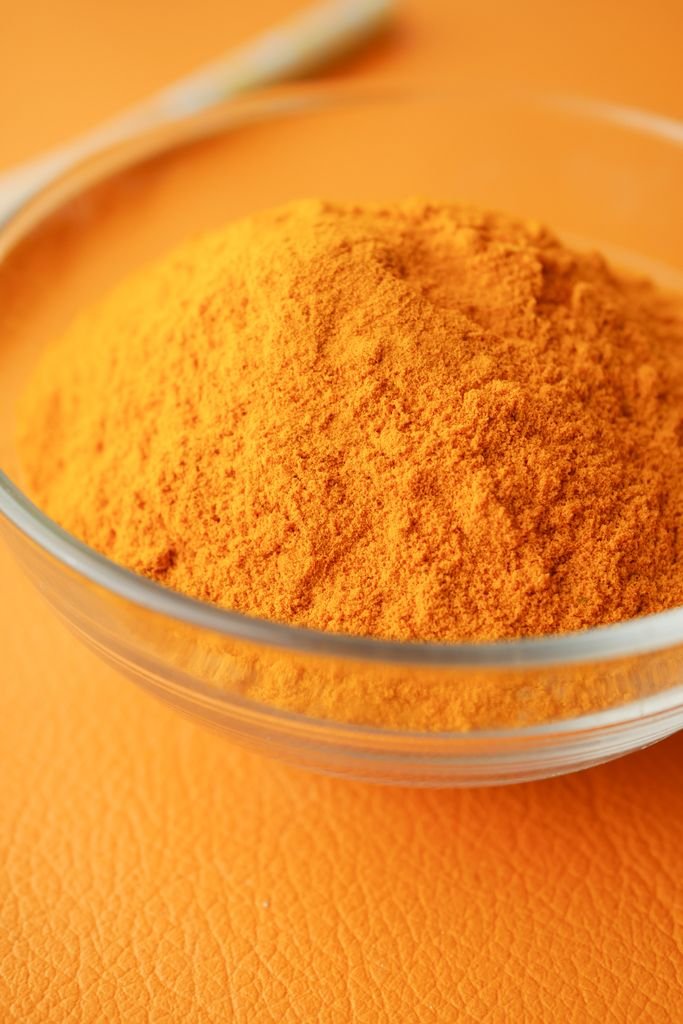 Close-up of bright turmeric powder in a glass bowl on an orange background, highlighting vibrant color contrast.